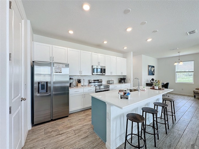 kitchen with a center island with sink, white cabinetry, appliances with stainless steel finishes, a kitchen breakfast bar, and light hardwood / wood-style floors