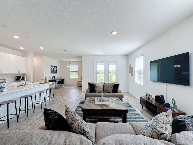 living room with light wood-type flooring, a textured ceiling, french doors, and sink