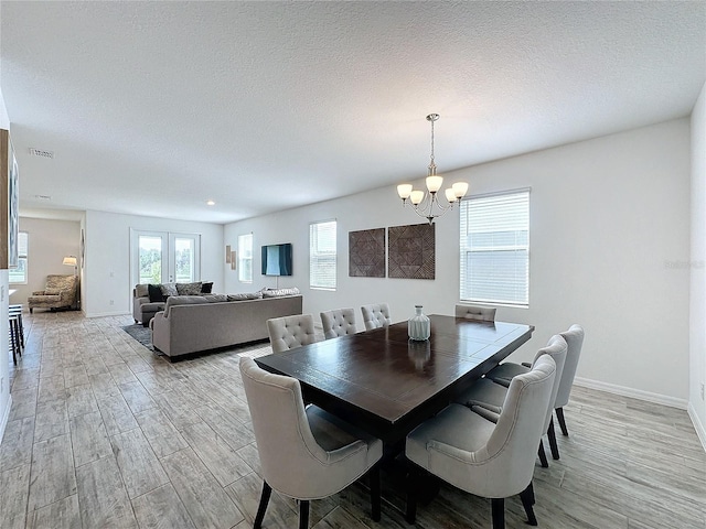 dining room with light hardwood / wood-style flooring, a textured ceiling, and an inviting chandelier