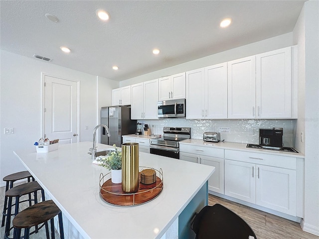 kitchen featuring appliances with stainless steel finishes, tasteful backsplash, an island with sink, white cabinets, and a kitchen bar