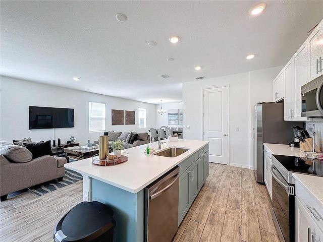 kitchen featuring a center island with sink, sink, a textured ceiling, appliances with stainless steel finishes, and white cabinets