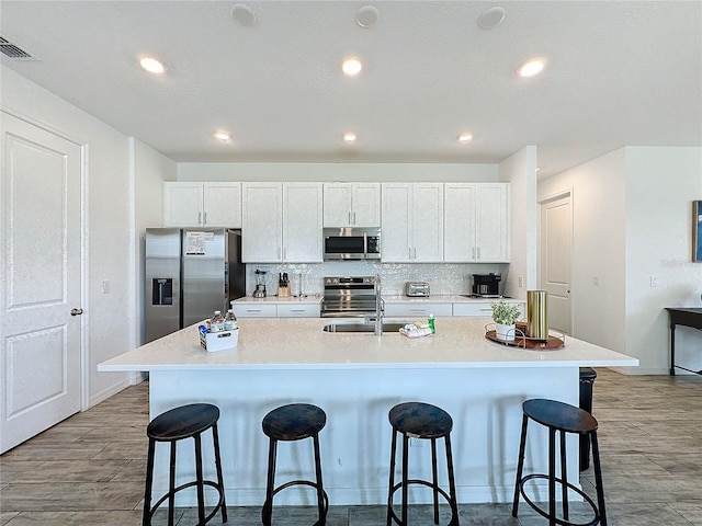 kitchen featuring appliances with stainless steel finishes, a kitchen breakfast bar, white cabinets, an island with sink, and decorative backsplash