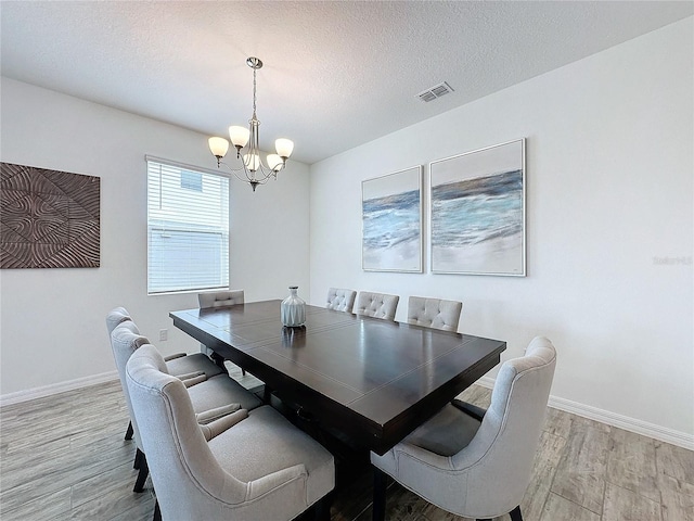 dining room featuring light wood-type flooring, a textured ceiling, and an inviting chandelier