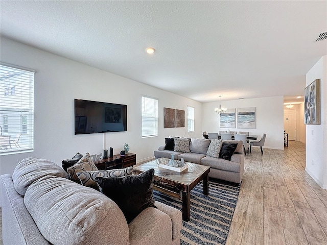 living room with light wood-type flooring, a textured ceiling, and a notable chandelier