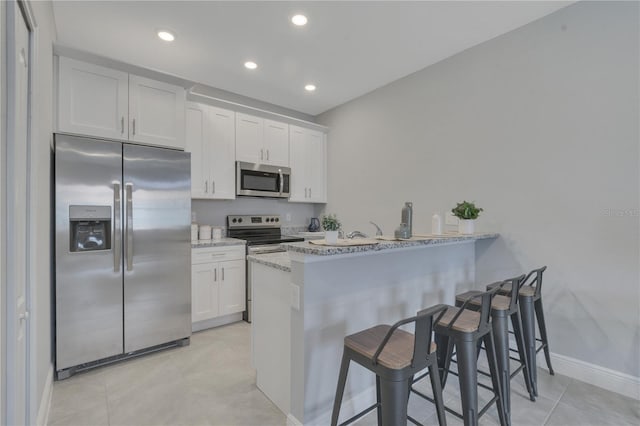 kitchen with light stone counters, white cabinets, kitchen peninsula, stainless steel appliances, and a breakfast bar