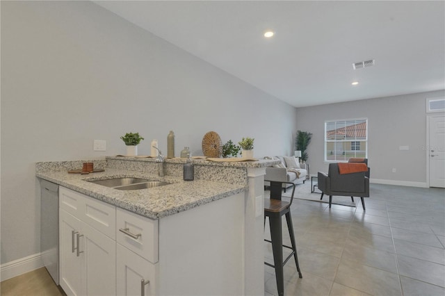 kitchen with light stone countertops, white cabinets, a kitchen breakfast bar, and sink