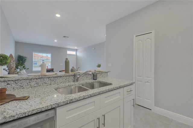 kitchen with light stone counters, white cabinets, light tile patterned floors, sink, and stainless steel dishwasher