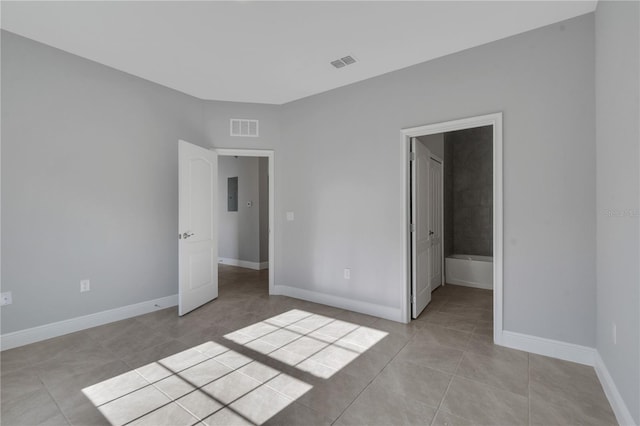 unfurnished bedroom with light tile patterned flooring, ensuite bath, and electric panel