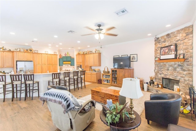 living room featuring a fireplace, ceiling fan, light wood-type flooring, and ornamental molding