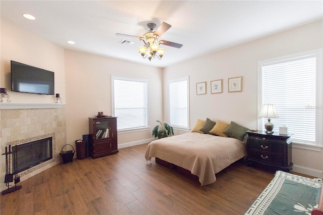 bedroom with ceiling fan, wood-type flooring, and a tile fireplace