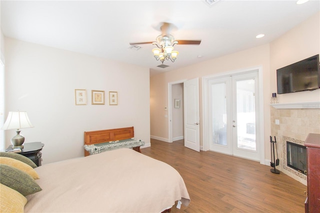 bedroom featuring access to exterior, french doors, ceiling fan, wood-type flooring, and a fireplace