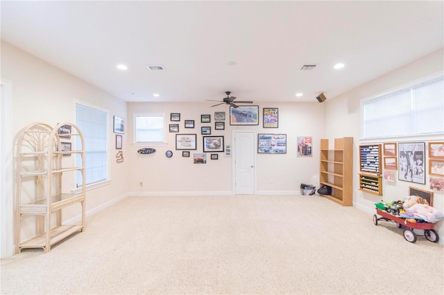 living area with a wealth of natural light, ceiling fan, and light carpet