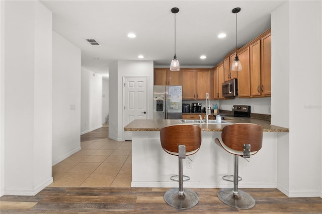 kitchen with pendant lighting, kitchen peninsula, appliances with stainless steel finishes, a breakfast bar area, and light wood-type flooring