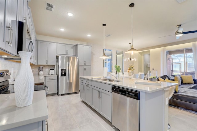 kitchen featuring a center island with sink, appliances with stainless steel finishes, hanging light fixtures, decorative backsplash, and ceiling fan with notable chandelier