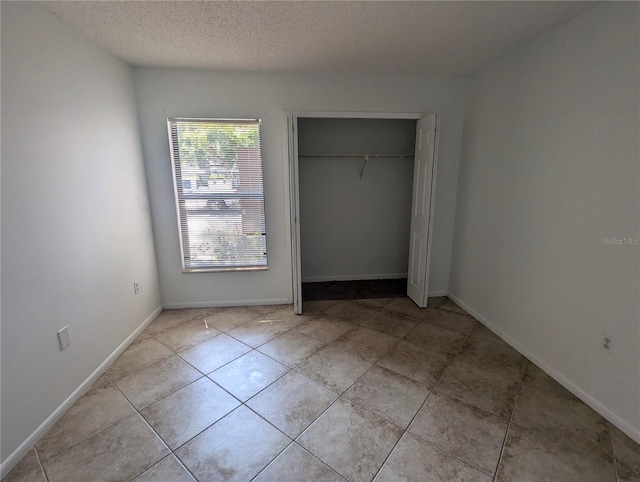 unfurnished bedroom with a textured ceiling, light tile patterned flooring, and a closet