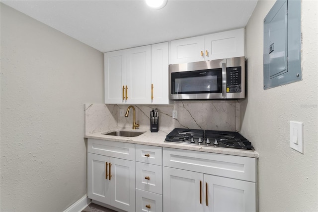 kitchen featuring electric panel, sink, tasteful backsplash, white cabinetry, and stainless steel appliances