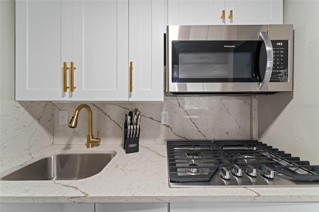 details featuring appliances with stainless steel finishes, decorative backsplash, light stone counters, and white cabinets