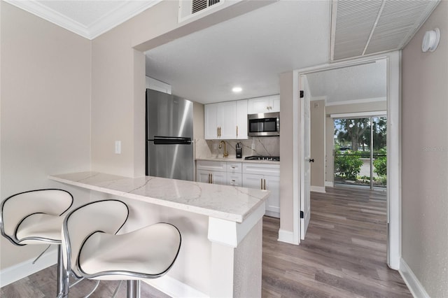 kitchen featuring white cabinets, appliances with stainless steel finishes, light hardwood / wood-style floors, and kitchen peninsula