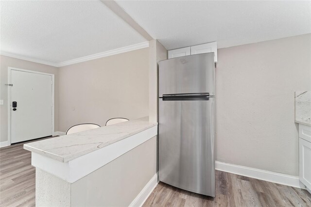 kitchen featuring stainless steel fridge, light hardwood / wood-style floors, white cabinetry, kitchen peninsula, and crown molding