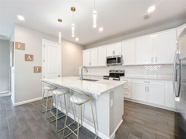 kitchen with decorative light fixtures, an island with sink, stainless steel appliances, and white cabinetry