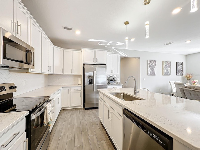 kitchen with stainless steel appliances, white cabinetry, decorative light fixtures, and sink