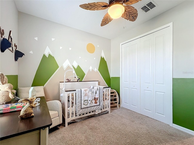 carpeted bedroom featuring a crib, ceiling fan, and a closet