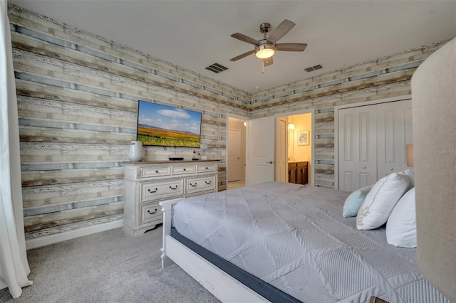 carpeted bedroom featuring ceiling fan, ensuite bath, and wood walls