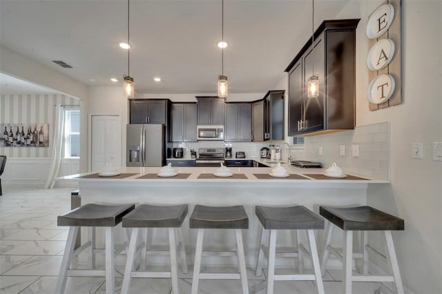 kitchen with appliances with stainless steel finishes, backsplash, kitchen peninsula, a kitchen bar, and decorative light fixtures