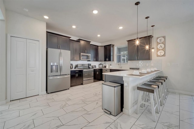 kitchen with sink, kitchen peninsula, a kitchen breakfast bar, stainless steel appliances, and decorative light fixtures