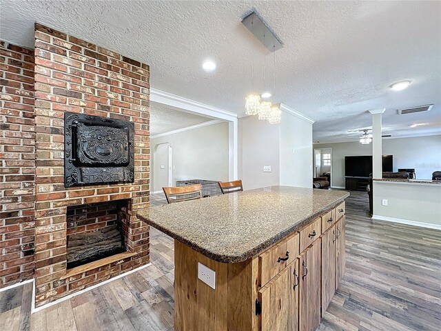 kitchen featuring a brick fireplace, ceiling fan, a textured ceiling, a kitchen island, and crown molding