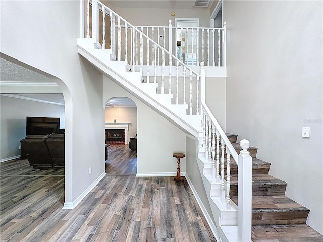 stairway with a high ceiling, wood-type flooring, and ornamental molding