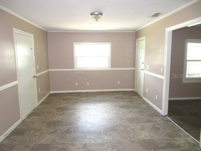 empty room with baseboards, visible vents, and crown molding