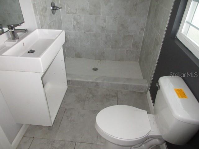 bathroom with tile patterned floors, vanity, toilet, and a tile shower