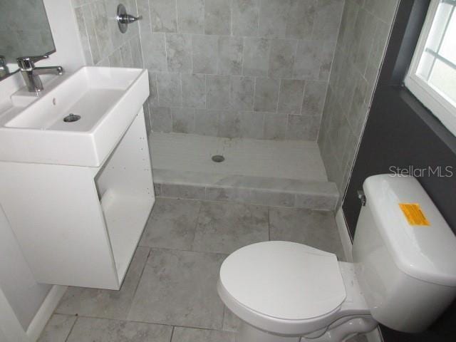 bathroom featuring toilet, vanity, and tiled shower