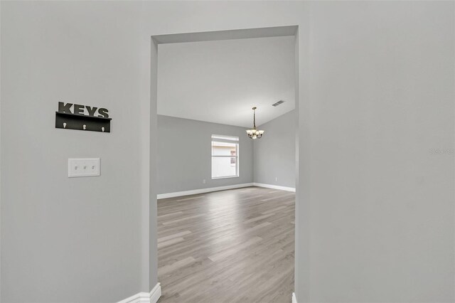 corridor with wood-type flooring and an inviting chandelier