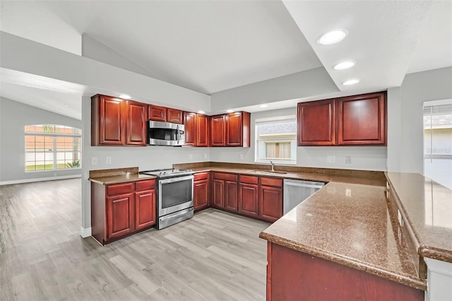 kitchen with light wood-type flooring, dark stone countertops, vaulted ceiling, and stainless steel appliances