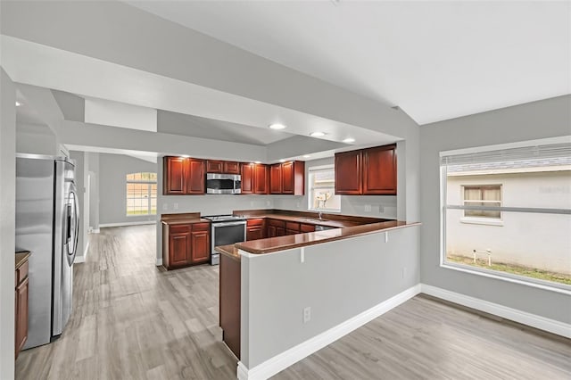 kitchen with light hardwood / wood-style floors, vaulted ceiling, stainless steel appliances, and kitchen peninsula