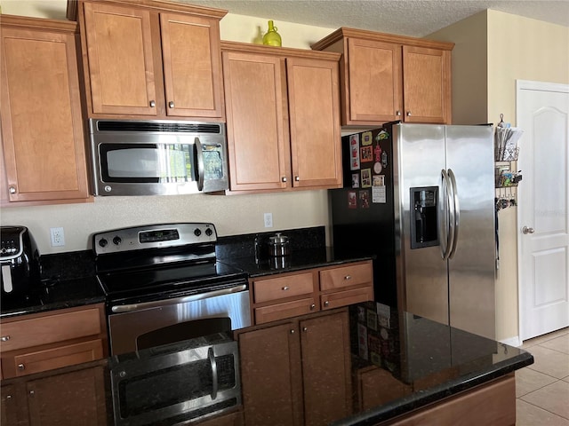 kitchen featuring light tile patterned flooring, stainless steel appliances, a textured ceiling, and dark stone counters