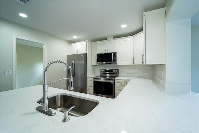 kitchen with white cabinets, sink, appliances with stainless steel finishes, light stone countertops, and decorative backsplash