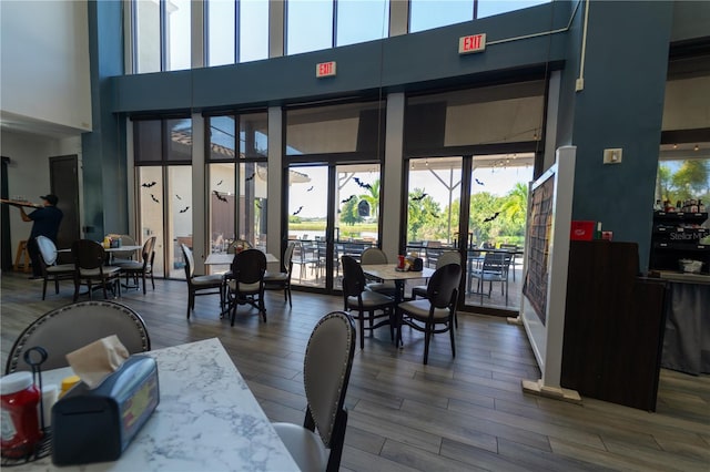 dining area featuring wood-type flooring, a towering ceiling, and french doors