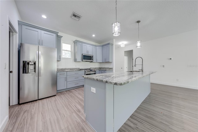 kitchen with a kitchen island with sink, stainless steel appliances, light stone countertops, pendant lighting, and a textured ceiling