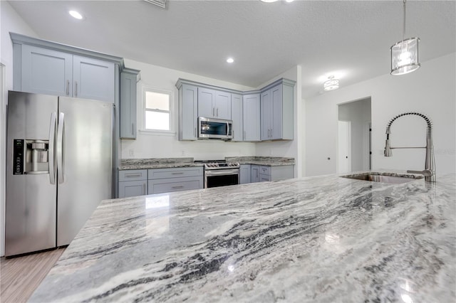 kitchen featuring appliances with stainless steel finishes, sink, light stone counters, and pendant lighting