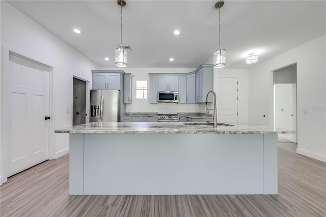 kitchen with decorative light fixtures, a kitchen island with sink, stainless steel appliances, and sink