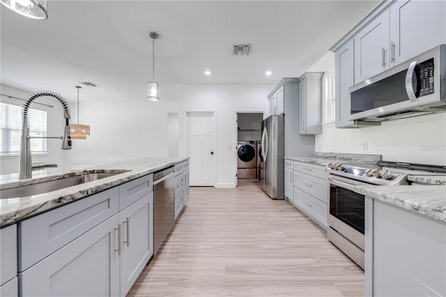 kitchen with appliances with stainless steel finishes, light stone countertops, separate washer and dryer, light hardwood / wood-style floors, and sink