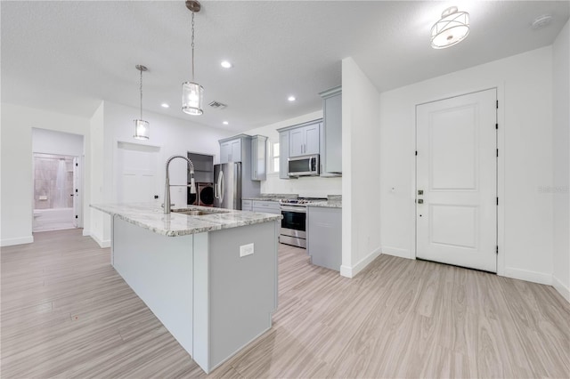 kitchen featuring gray cabinetry, appliances with stainless steel finishes, decorative light fixtures, light hardwood / wood-style flooring, and a center island with sink