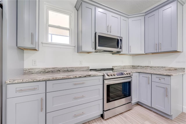 kitchen with light hardwood / wood-style flooring, stainless steel appliances, gray cabinets, light stone counters, and a textured ceiling