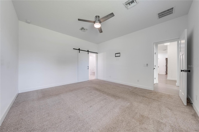 spare room with a barn door, light colored carpet, and ceiling fan