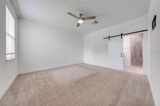 carpeted spare room featuring a barn door and ceiling fan