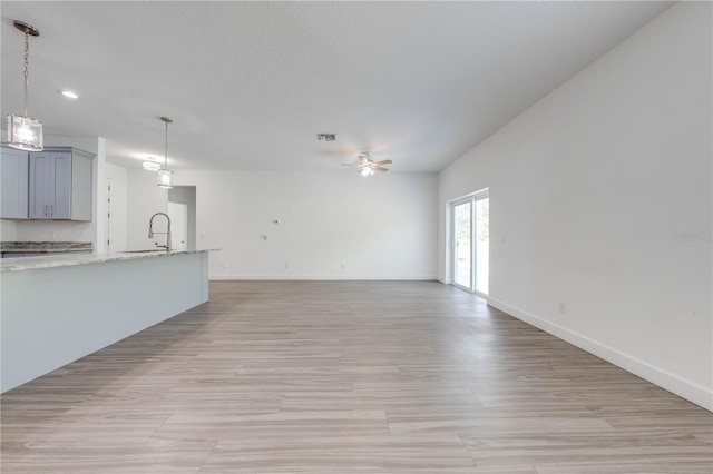 unfurnished living room featuring visible vents, baseboards, a ceiling fan, and a sink