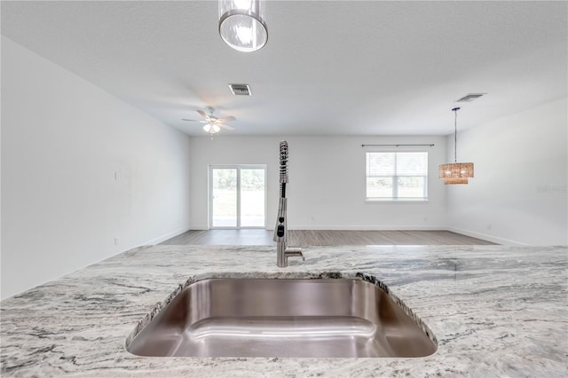 kitchen with visible vents, a sink, light stone counters, open floor plan, and hanging light fixtures